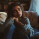 woman on couch, eyes gazing into distance with worried expression